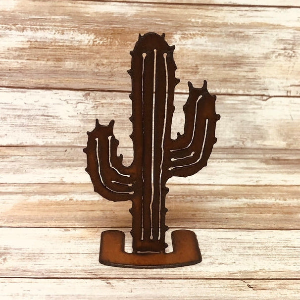 Rusty metal cutout standee of a tall saguaro cactus with multiple arms on a curved base against a wood background