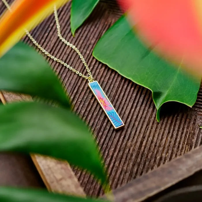 Close-up of Paradise Island reversible bar necklace pendant on wood with pink flower and turquoise tropical print.