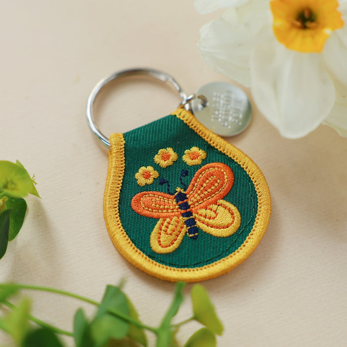 Green teardrop patch keychain with yellow border and embroidered butterfly and flowers on a metal keyring