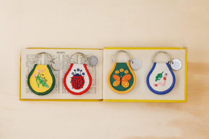 Four colorful embroidered patches featuring a ladybug dragonfly flamingo and grasshopper on a vintage display card