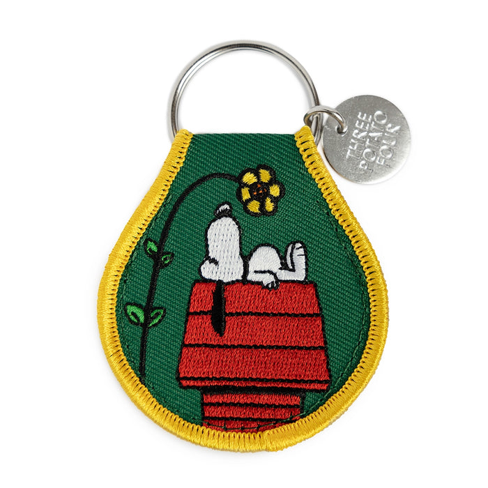 Snoopy doghouse flower patch keychain on green fabric with a yellow border.