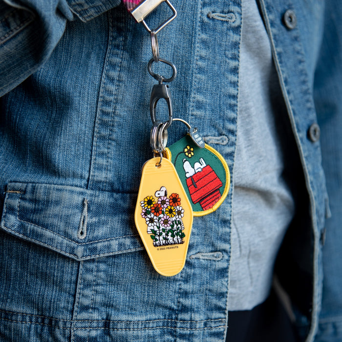Denim jacket shows a two patch Peanuts keychain set featuring a yellow flower patch and a Snoopy doghouse patch.