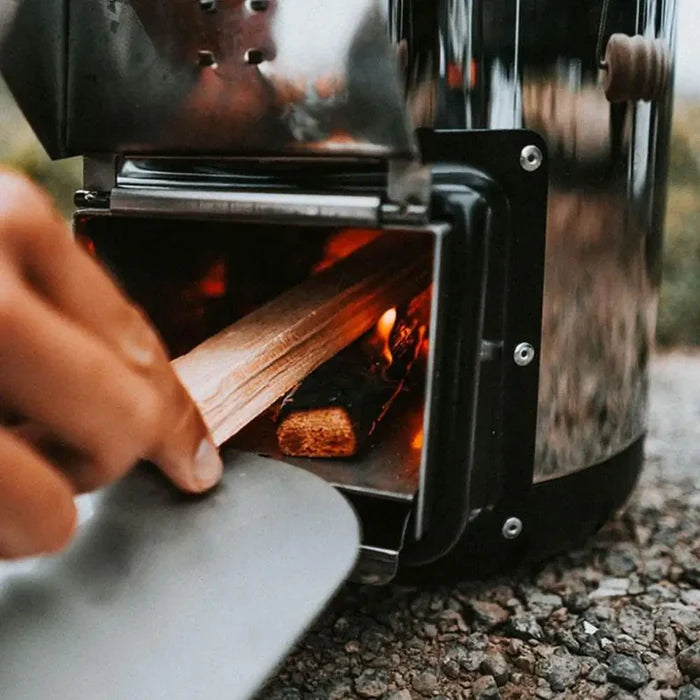 Lifestyle shot of a person feeding wood in to the combustion chmaber of a Petromax Rocket stove RF33