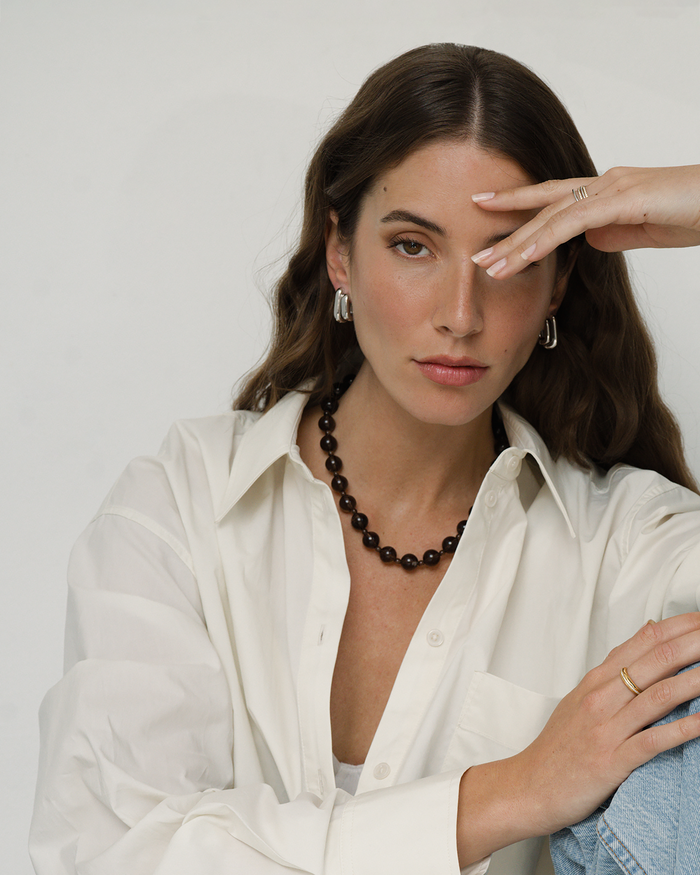 Woman wearing a white shirt and black beaded necklace against a plain background