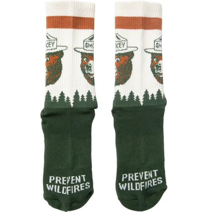 Pair of crew socks with white upper, orange stripe at the top, forest edge design and green foot with Prevent Wildfires on the toe.