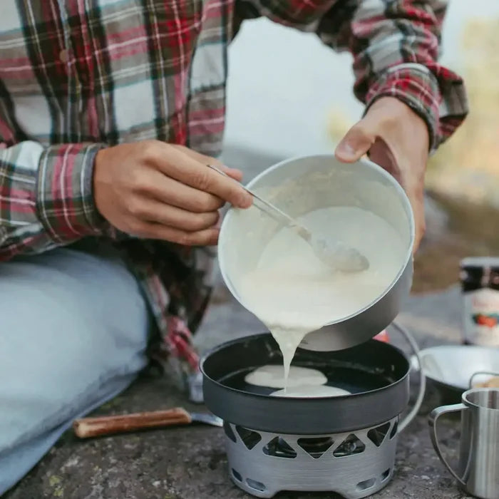Lifestyle image of a man outdoors cokking pancakes on his Primus Essential stove set in 1300ml size