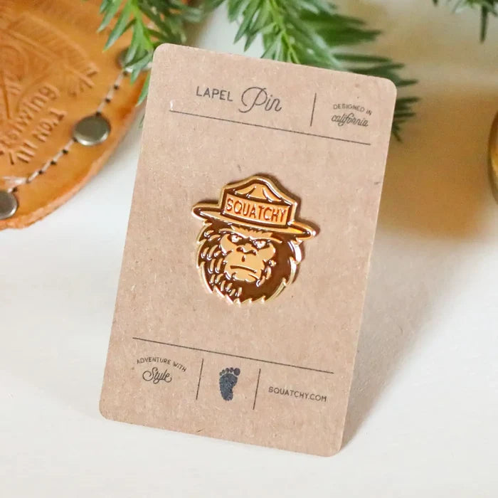 Ranger Squatchy enamel pin mounted on a brown kraft lapel pin display card