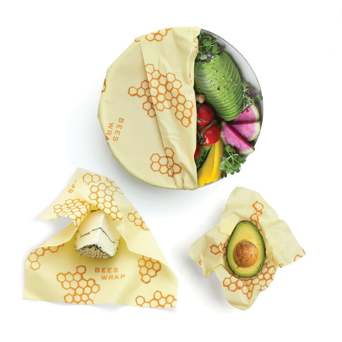Assorted sized beeswax wraps in pale yellow with hexagon print covering a bowl of fresh vegetables