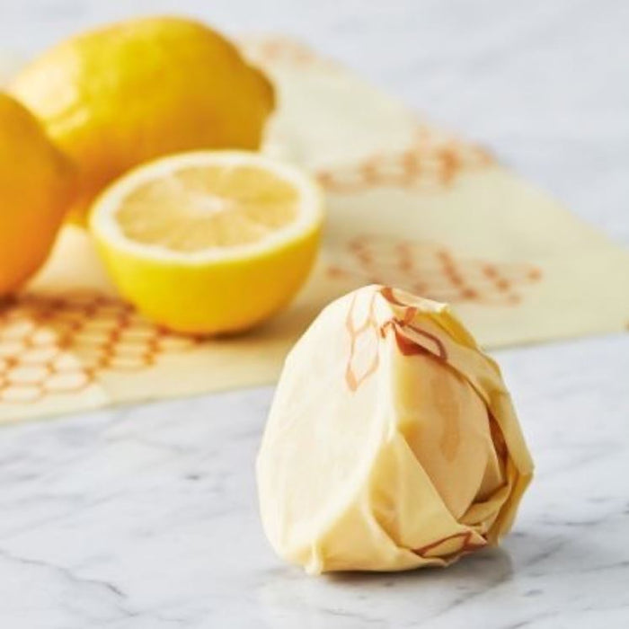 Beeswax wrap wrapped around a round cheese ball on a marble surface with lemons in the background