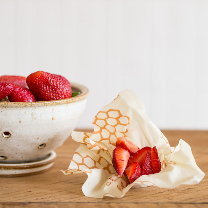 Beeswax wrap with hexagon pattern wrapping fresh strawberries on a wooden table