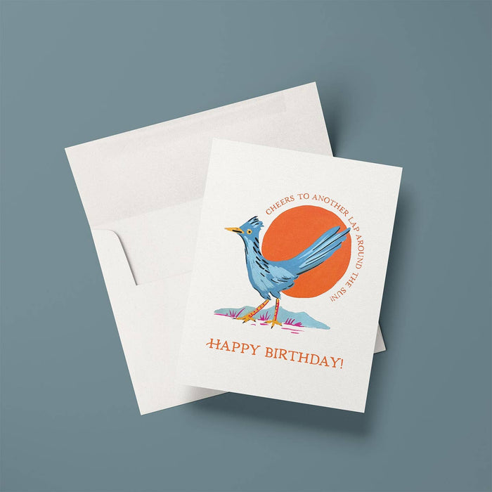Roadrunner Birthday Card with blue roadrunner standing before an orange sun and Happy Birthday text on a white card with an envelope.