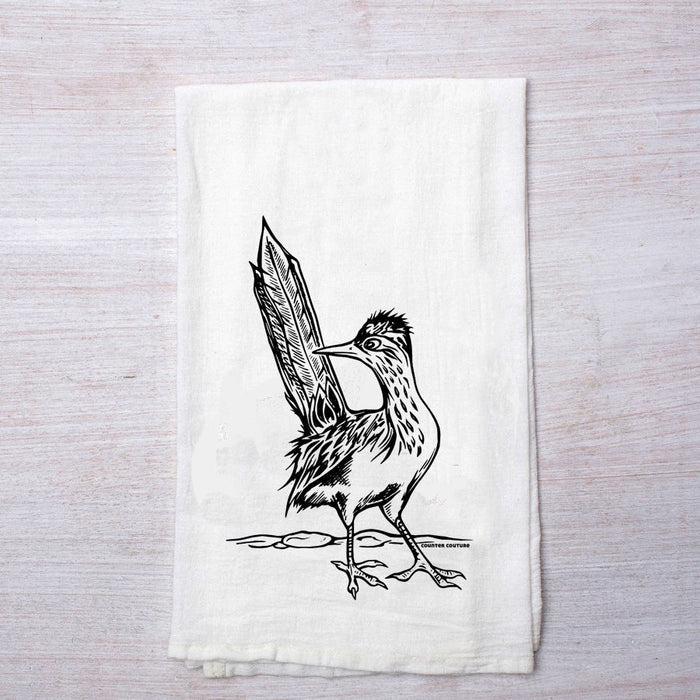 White tea towel with a roadrunner illustration laid on light wood background