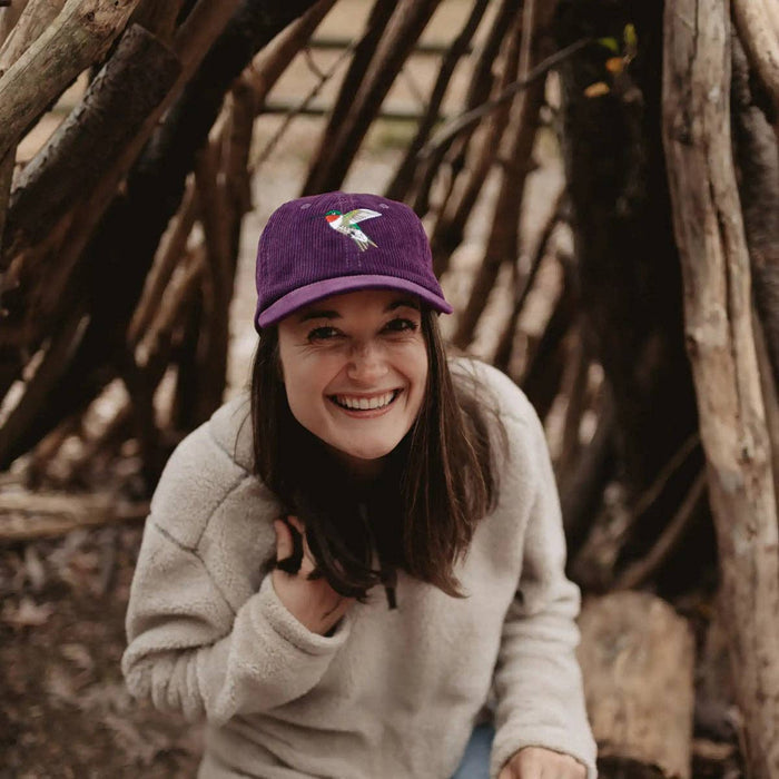 Smiling woman wearing a purple corduroy Ruby-throated hummingbird hat.