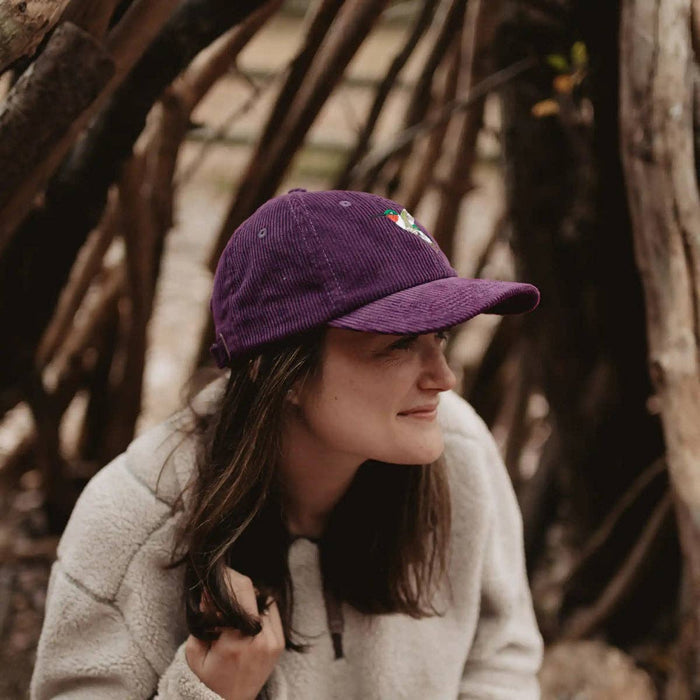Side profile of a woman wearing a purple corduroy hummingbird hat with an embroidered design.