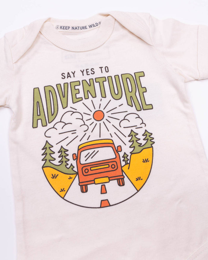 Detail of the adventure graphic on the pale pink onesie with a red car, winding road, mountains and trees