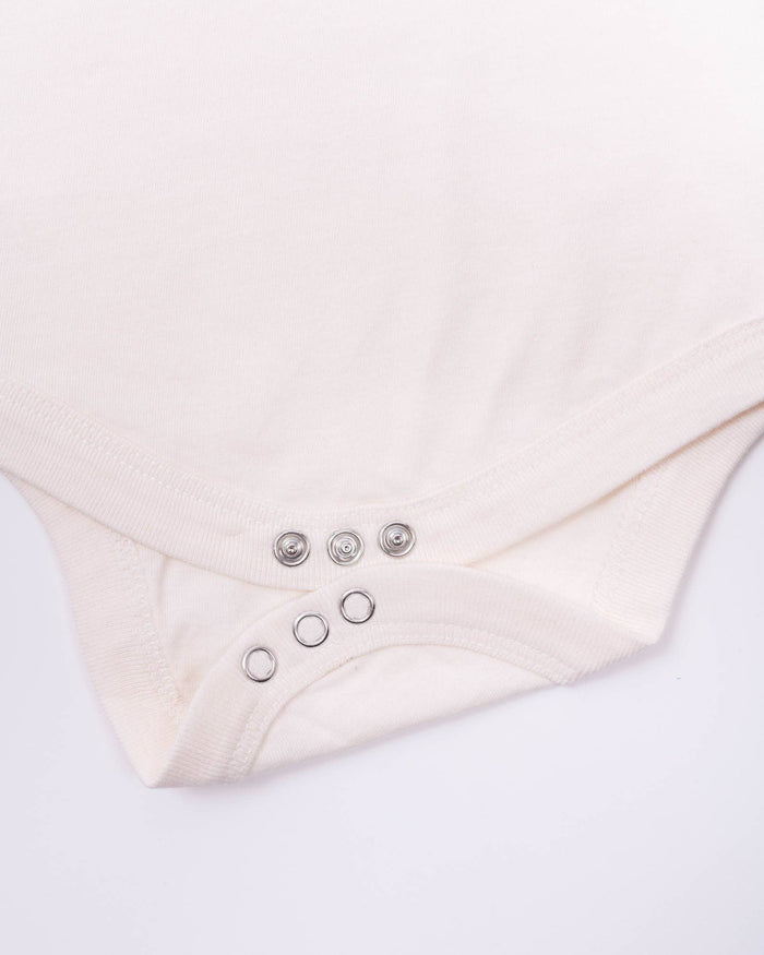 Soft pink baby onesie close up showing snap buttons along the bottom edge.