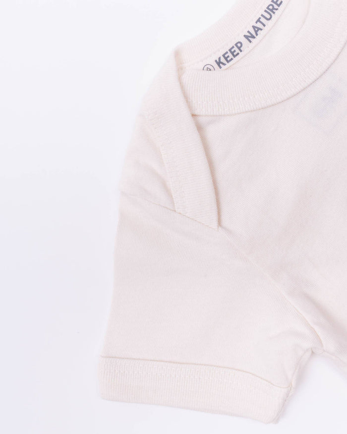 Cream onesie with a green Keep Nature Wild tag at the side seam.