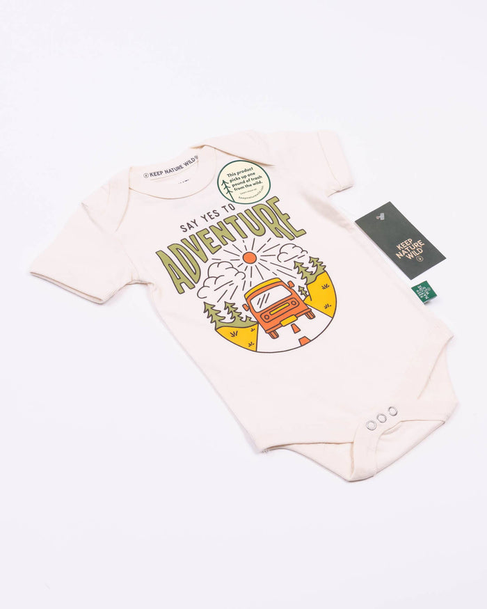 Cream baby onesie with bold adventure graphic featuring a sun mountains and a retro bus