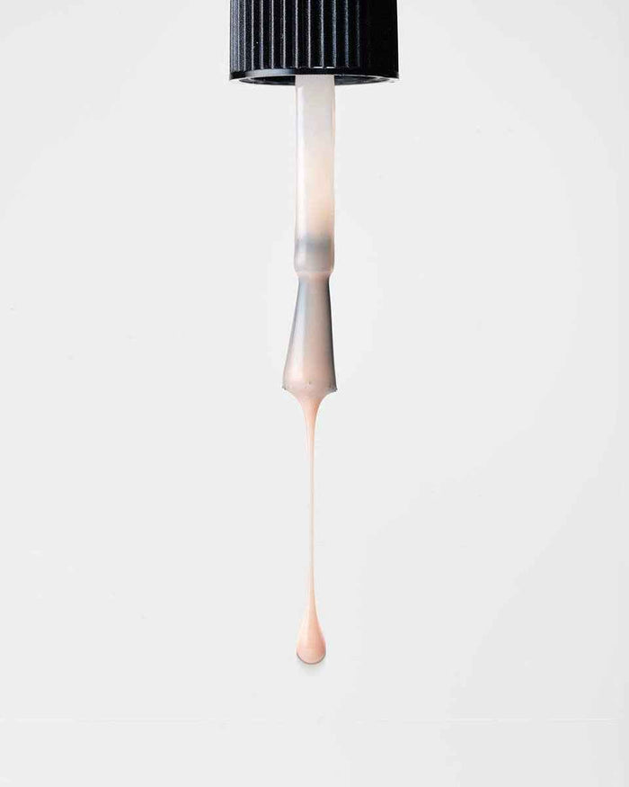 Nail polish brush with beige polish dripping on a white background