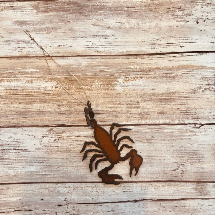 Rusty scorpion metal ornament hanging from twine on weathered wooden background