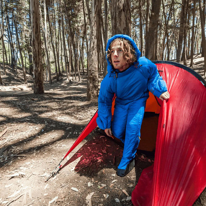 Lifestyle shot of a man camping in the woods leaving his tent wearing a Selk'Bag original 6G sleeping bag suit
