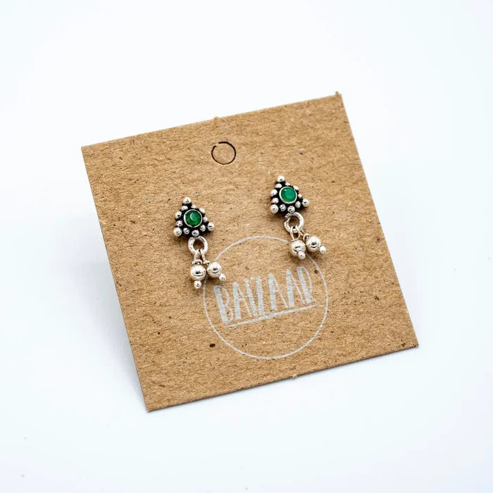 Silver emerald charm stud earrings with green cabochon and beaded halo on a kraft display card