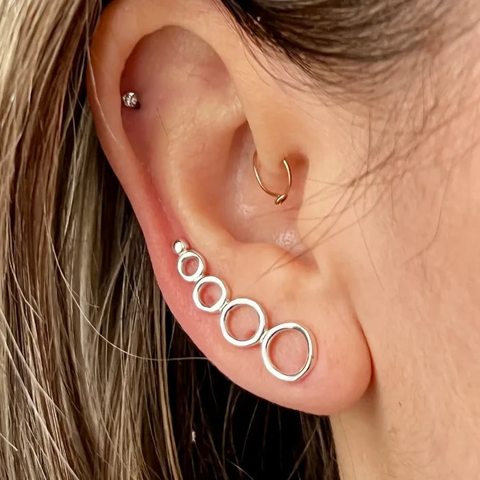 Close up of ear with a diamond stud a small gold hoop and a silver stacked circle earring along the lobe