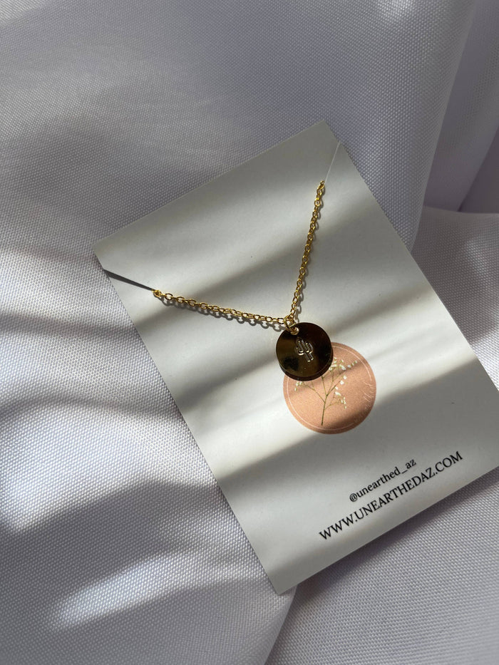 Gold chain necklace with a round pendant resting on a white card against pale fabric
