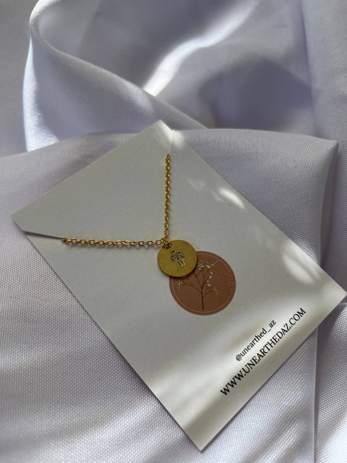 Gold tone necklace with a circular pendant and cutout detail displayed on a white folded card