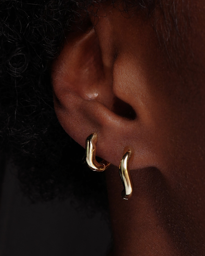 Close-up of a person wearing the Sloan Wavy Huggies earrings, showcasing their unique, modern design.