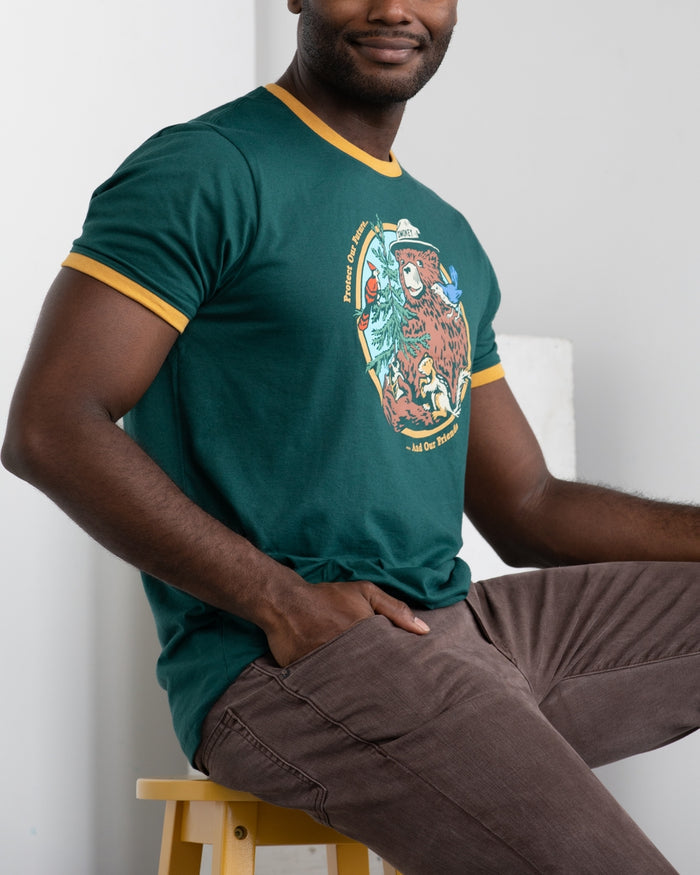 Male model wearing Smokey's Friends Ringer Tee in deep green with mustard trim, front view showing the graphic.