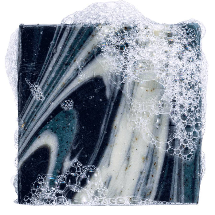 Close up of Snowy Pine Tar soap bar with dark blue and white marbling and bubbles.
