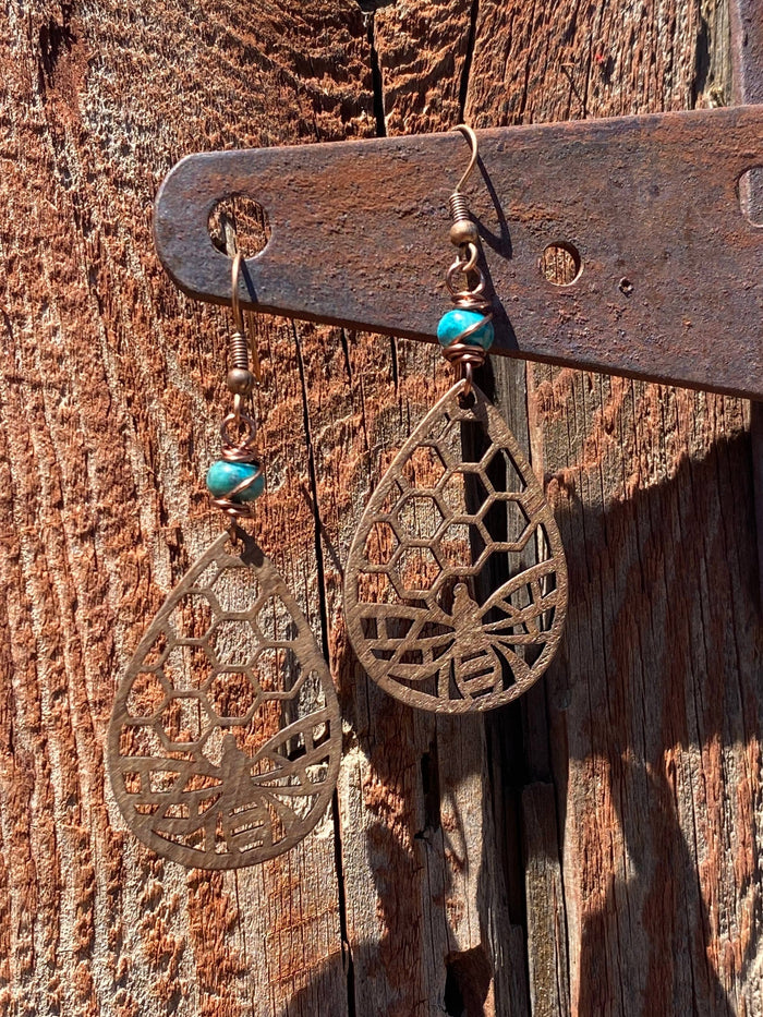 Turquoise bead wrapped in copper wire on a honeycomb earring against a rustic wooden backdrop