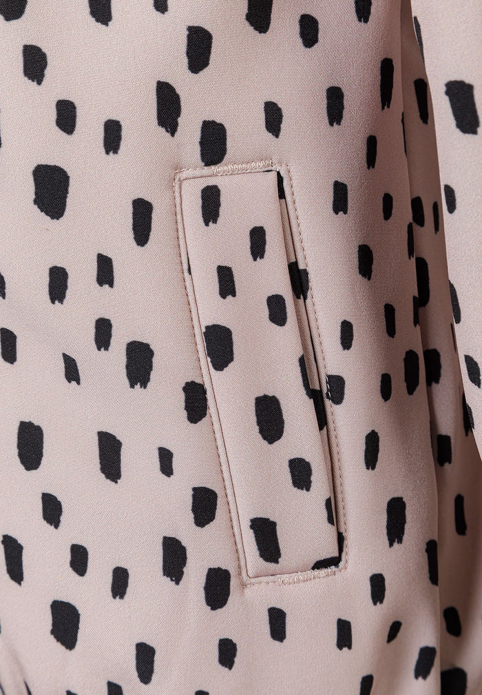Detail of a girls' softshell jacket in pink with black spots, featuring a front pocket.