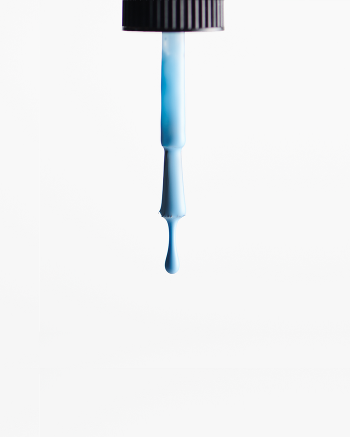 Blue nail polish being dripped from a nail polish application brush against a white background
