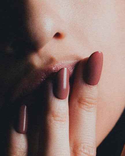 Close-up of a person's lips and nails with dusty rose-colored polish with a dark background