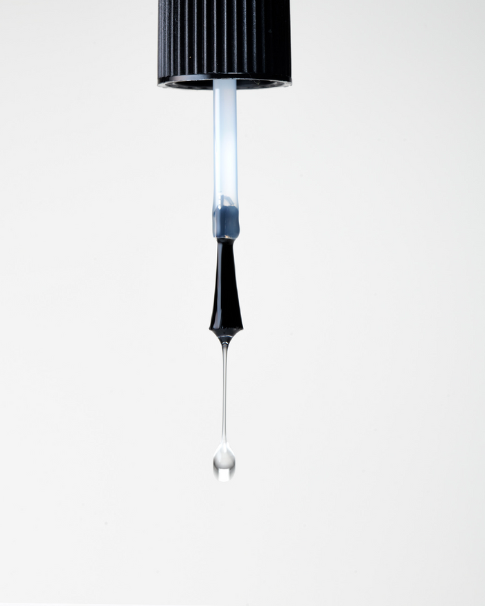 Clear nail polish being dripped from a nail polish application brush against a white background