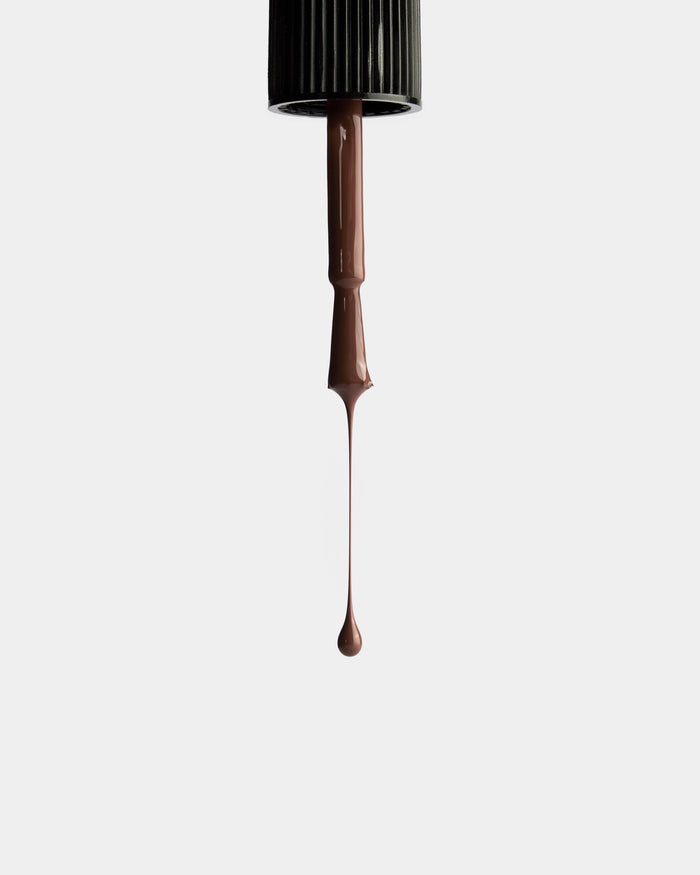 A Ssone Nail Lacquer brush coated in long-wearing, vegan brown polish forms a single drop at the tip, set against a plain white background.