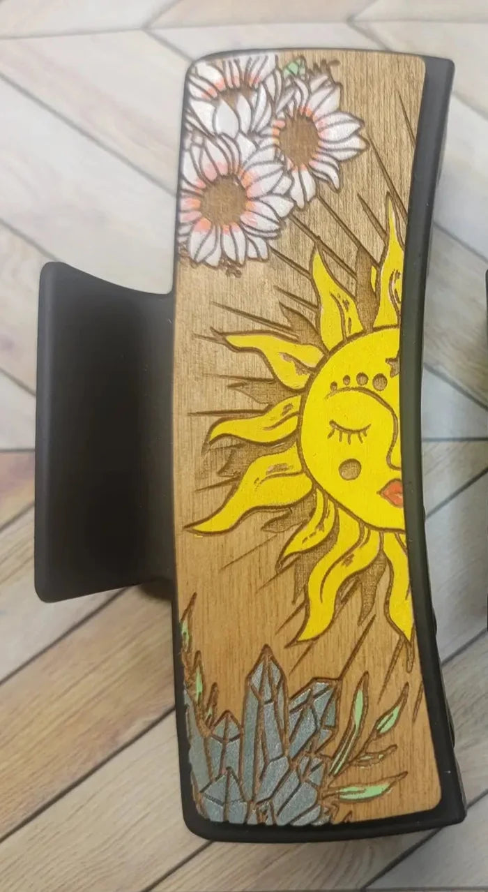 Wooden textured panel featuring a yellow sun, white daisies, and blue crystal accents on a black claw clip