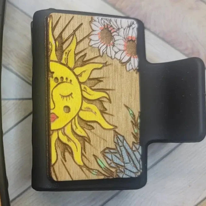 Wooden panel featuring a sun and daisies design on a black claw clip