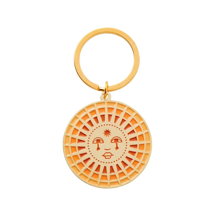 Sun enamel keychain close up showing a round pendant with lattice sun rays and a smiling face against an orange background.