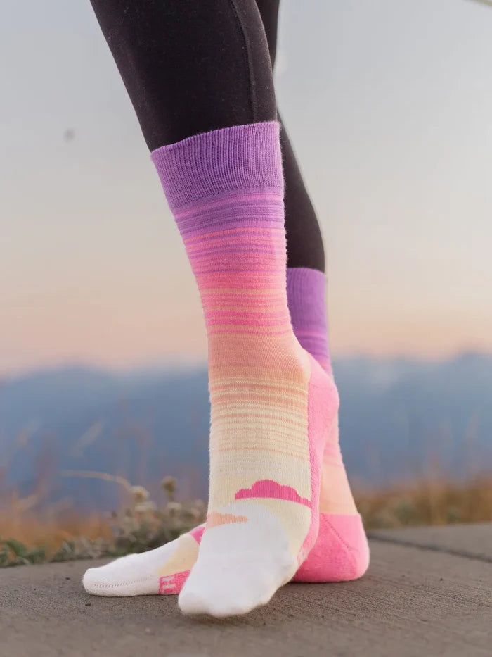 Sunrise Socks worn on a leg with a purple cuff and pink purple gradient pattern against a dark outfit