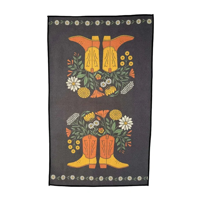 Western Bloom kitchen towel with two orange boots surrounded by flowers on a dark woven background.