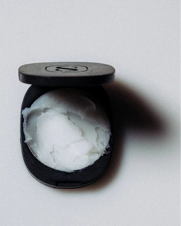Black compact with white cream inside on a light gray background