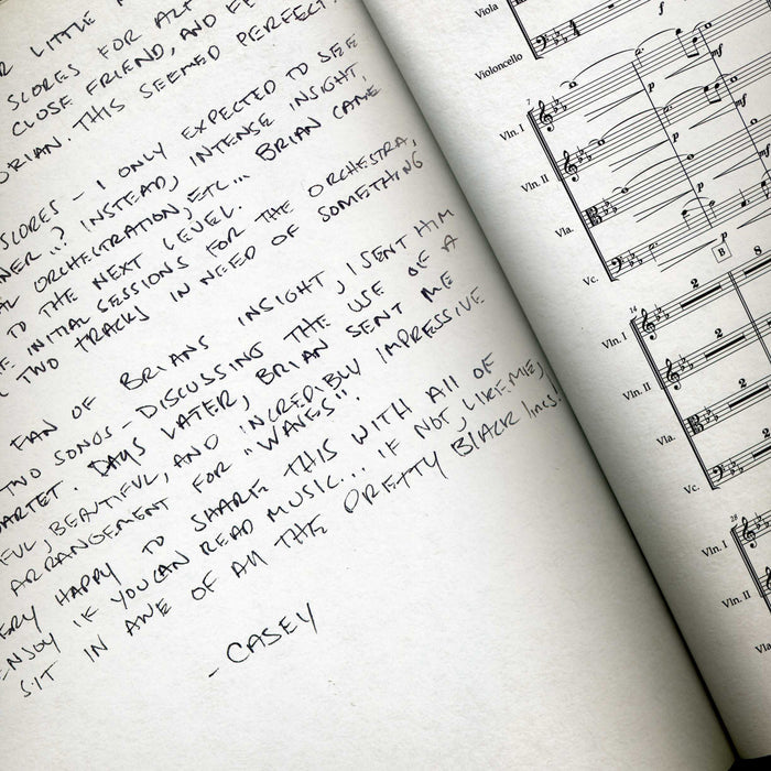 A handwritten note signed by Casey of The Dear Hunter rests beside open orchestral sheet music, sharing music reflections and admiration—a unique piece ideal for any coffee table book featuring artwork or photos.