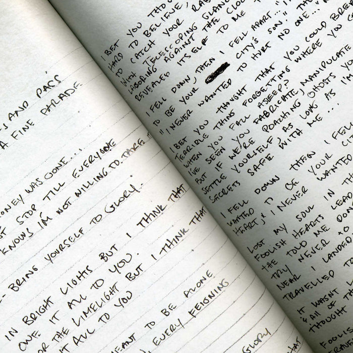 An open The Dear Hunter notebook displays dense, slightly slanted handwritten notes in black ink on both pages. The clean pages feature only text—no artwork, sketches, or photos are present, giving a personal journal-like feel.