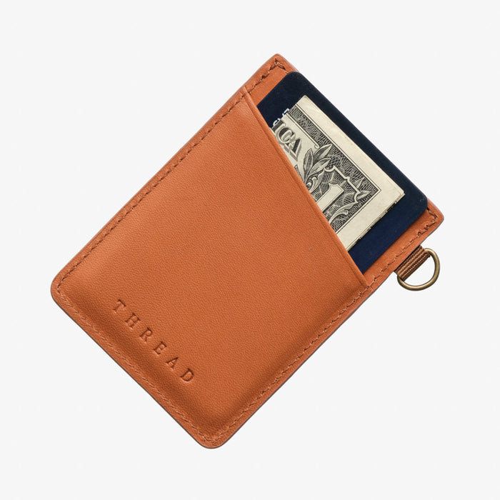 Tan leather compact card wallet with a navy card visible and a brass ring attachment