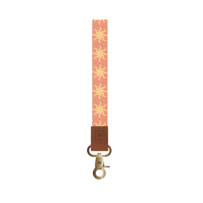 Thread patterned wrist lanyard in pink with yellow sunburst motifs, brown leather end and brass clasp