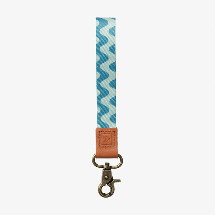 Blue and white zigzag thread wrist lanyard with tan leather tab and brass clip