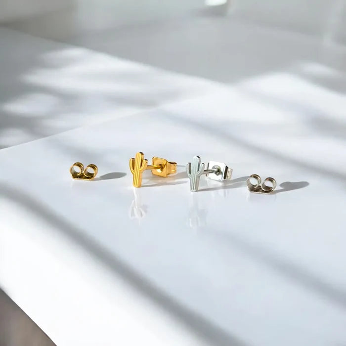 Assorted tiny desert cactus stud earrings in gold and silver finishes laid out on a white surface.